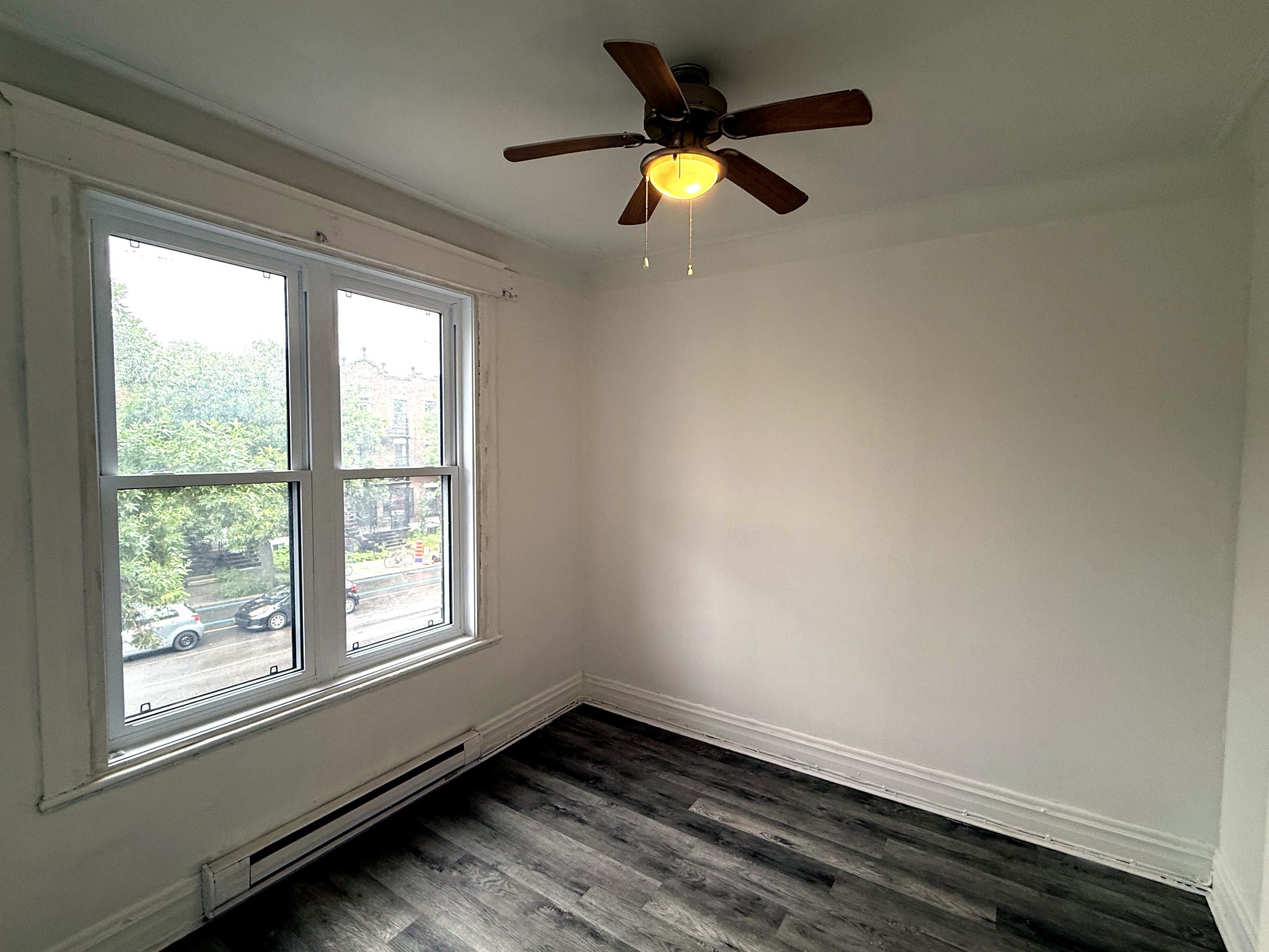 Pièce avant vide, grande fenêtre double sur la rue, ventilateur de plafond.