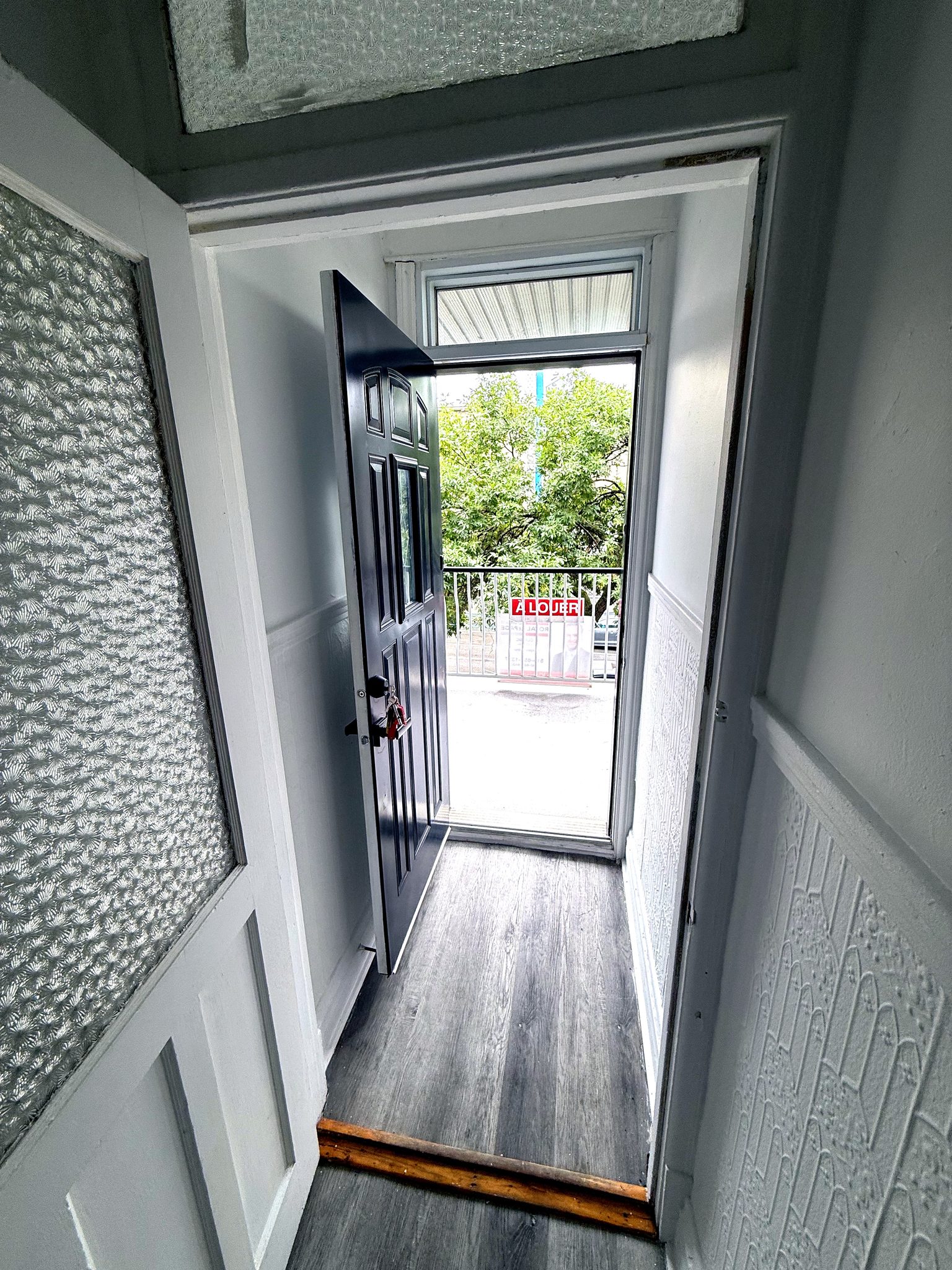 Entrée avant : porte noire ouverte sur le balcon et la rue.