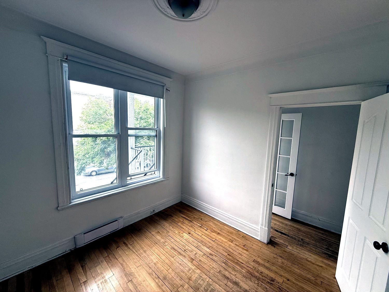 Chambre vide, fenêtre double donnant sur les arbres de la rue, plancher de bois franc.