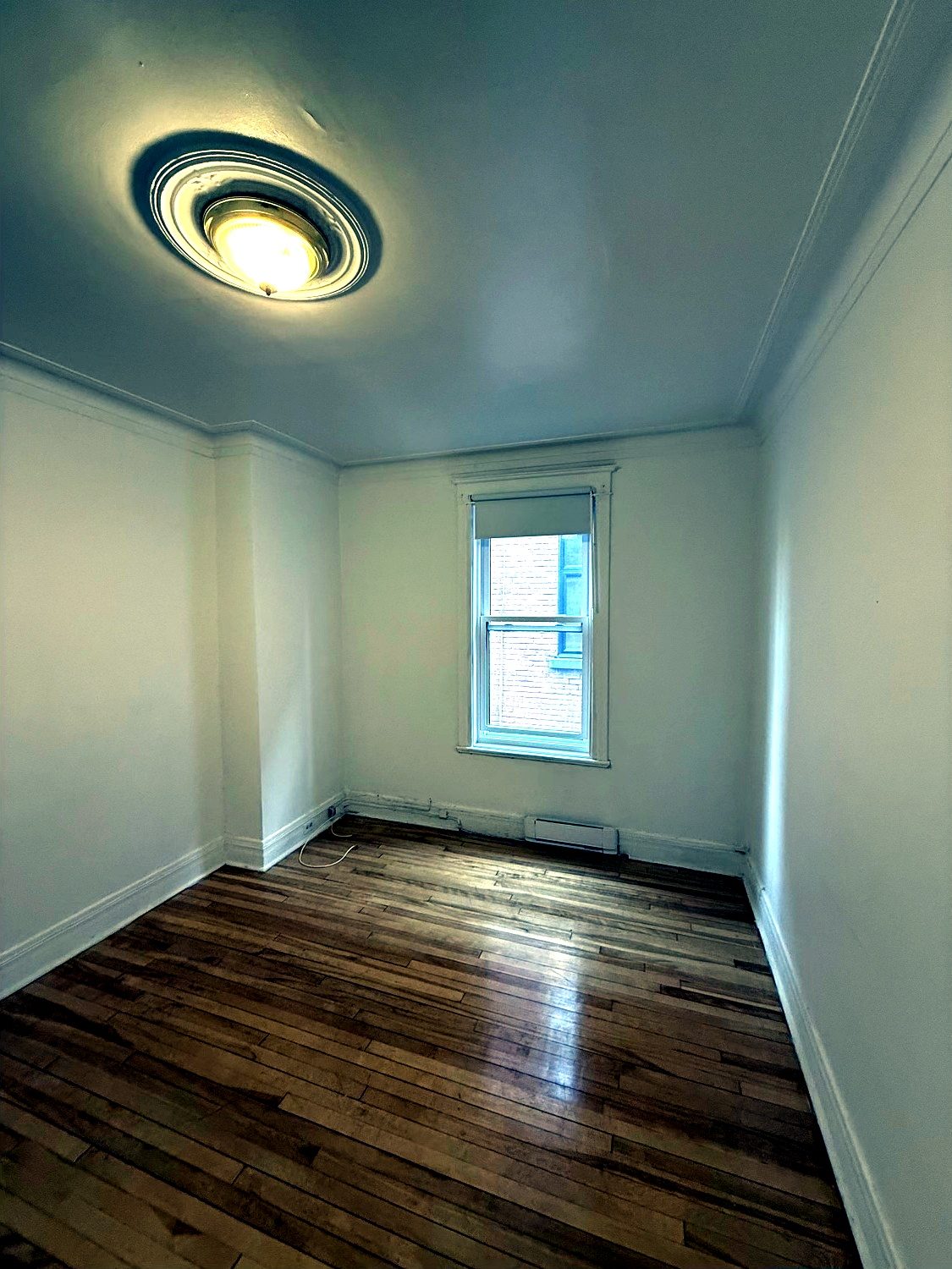 Deuxième chambre, fenêtre sur la brique voisine, plancher de bois foncé.