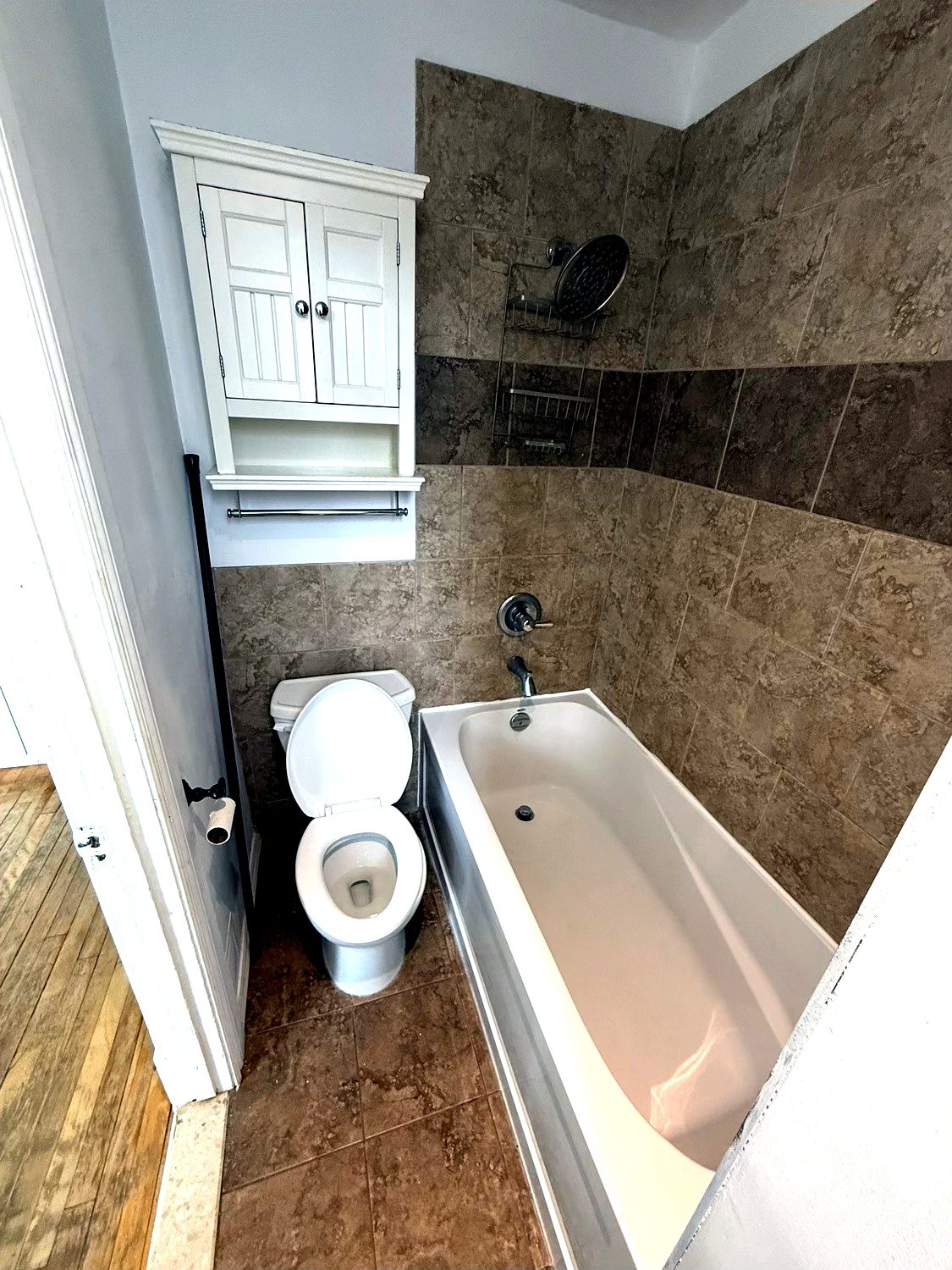 Salle de bain avec baignoire-douche et céramique brune pleine hauteur.