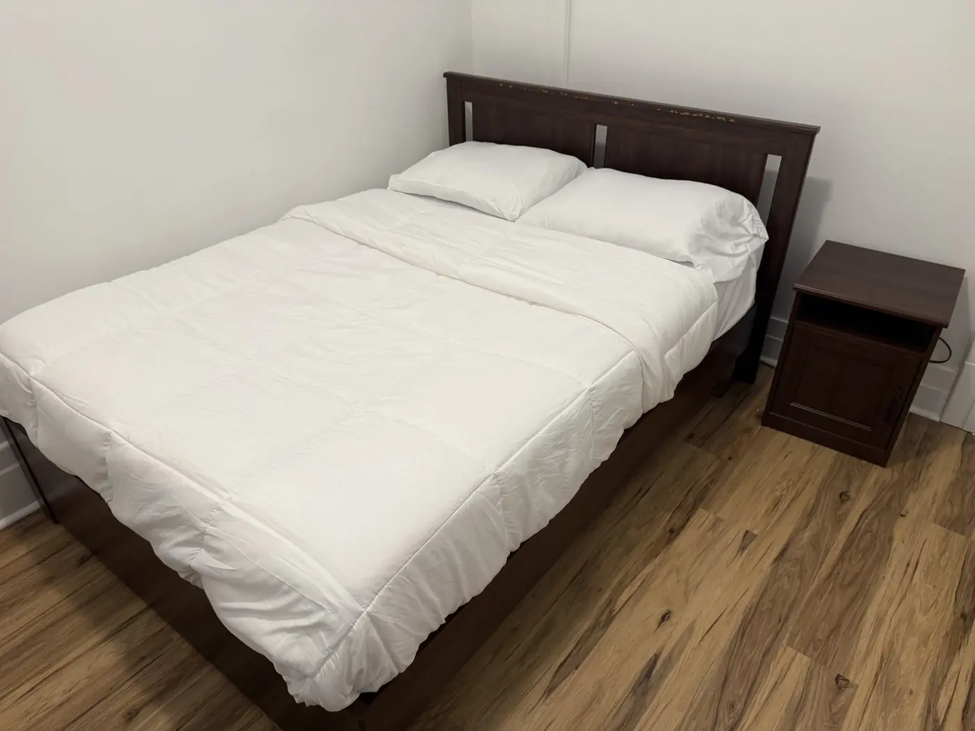 Chambre meublée avec lit queen et plancher de bois.