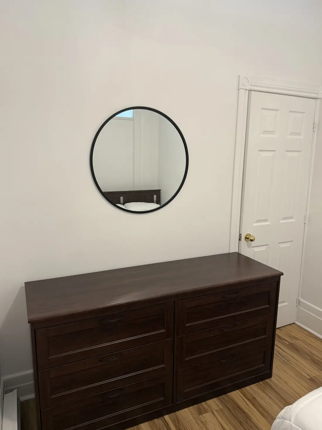 Commode en bois foncé surmontée d’un miroir rond.