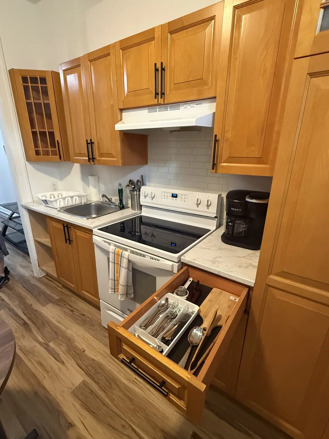 Coin cuisson : cuisinière, dosseret de céramique métro et tiroir à ustensiles ouvert.